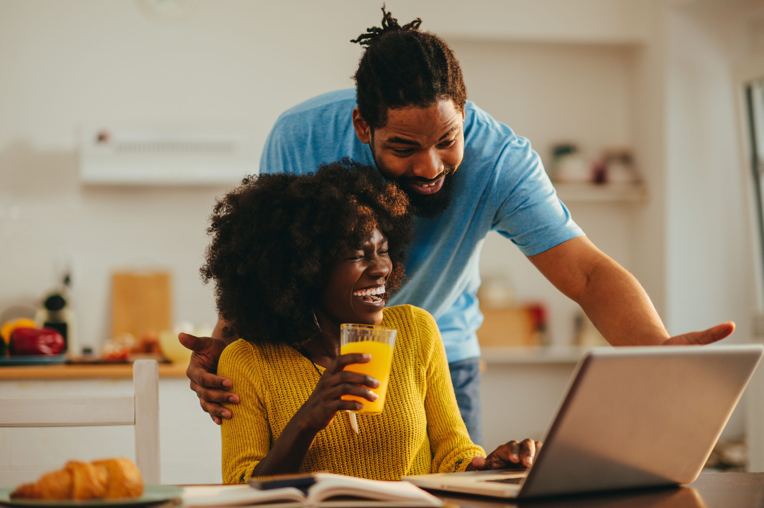 A happy african american couple is looking at the laptop and laughing at home together.