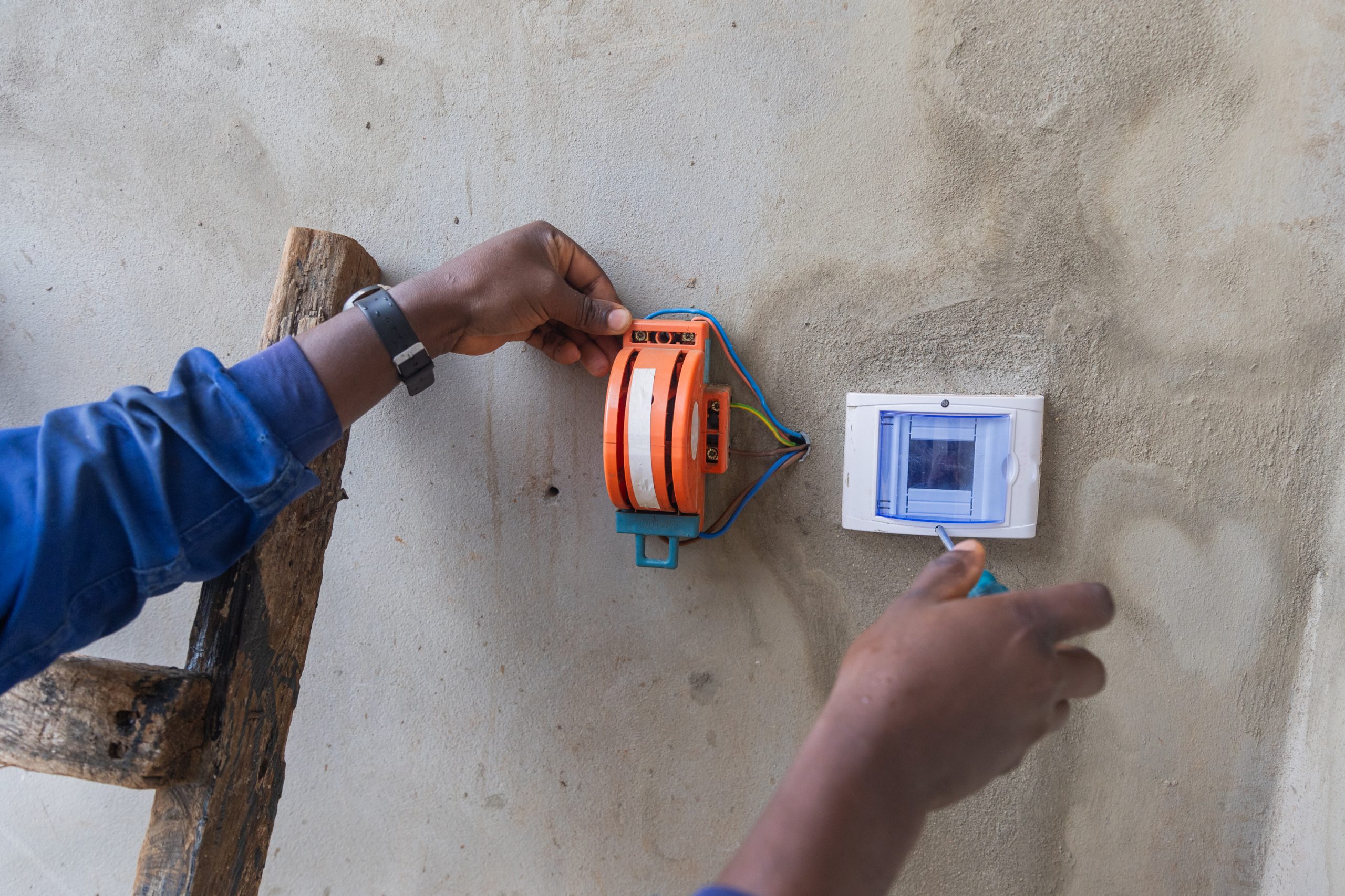 Foreground shot of an electrician’s hands on a ladder opening a box on the wall